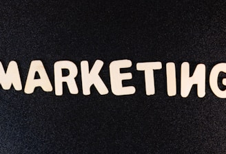 Wooden letters arranged to spell the word 'MARKETING' on a black textured background.