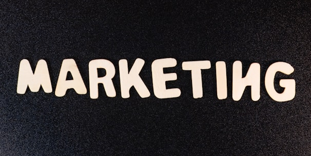 Wooden letters arranged to spell the word 'MARKETING' on a black textured background.